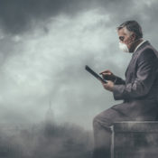 Man in business suit and a surgical mask works on his tablet while sitting in the thick of city smog.