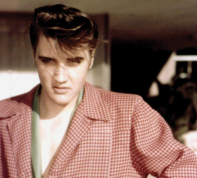 A young Elvis Presley poses for a photo wearing a red, checkered sports jacket.