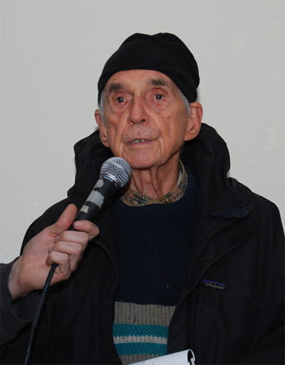 Daniel Berrigan speaking into a microphone as its held close to his face.