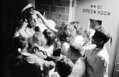 Elvis being grabbed by fans outside of a studio.