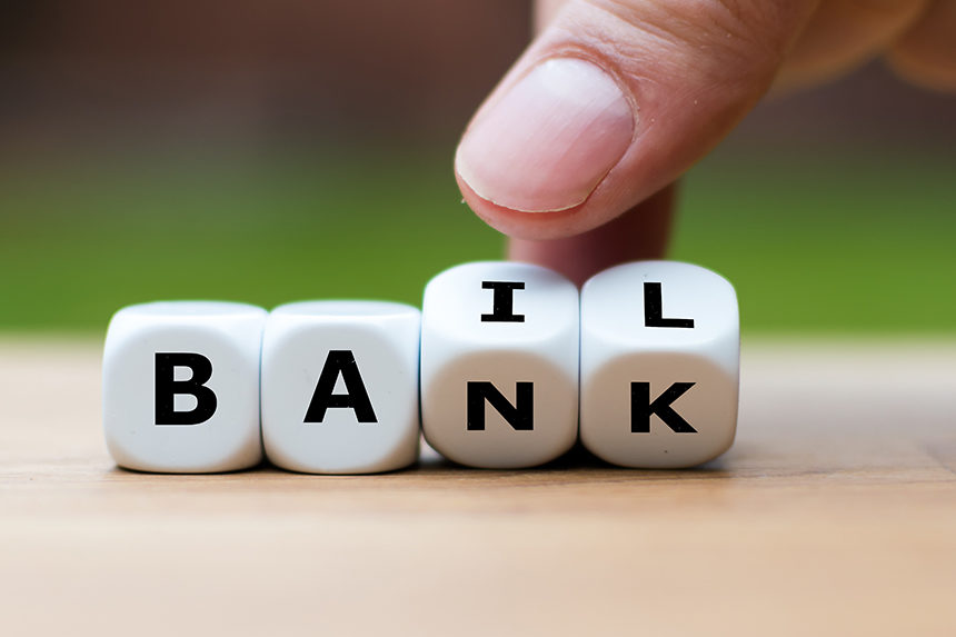 A string of beads with letters on them that spell out the word, "BANK." A human hand can be seen tipping over the letters "N" and "K", revealing the letters "I" and L" and the other side to spell out the word, "BAIL."