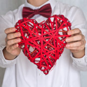 A person with a red bowtie holds a wicker Valentine heart