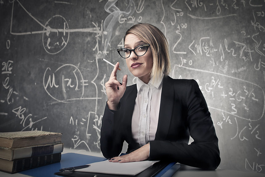 Teacher smoking a cigarette behind her classroom desk.