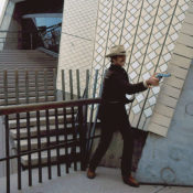 Actor Dennis Weaver fires a pistol outside an office building during an episode of the TV western, "McCloud".