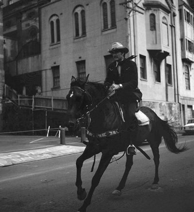 "McCloud" actor Dennis Weaver rides a horse down a city street.