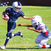 A young running back pushes an opposing team member out of the way during a game of youth football.