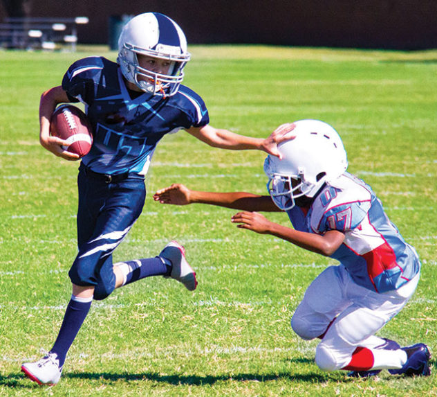A young running back pushes an opposing team member out of the way during a game of youth football.