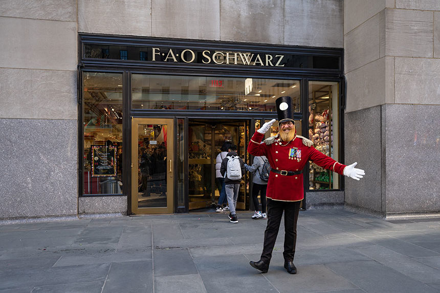 A man in a toy soldier costume salutes in front of a F.A.O Schwarz store