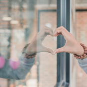 Woman forming a heart with her hand and its reflection in a glass store window.