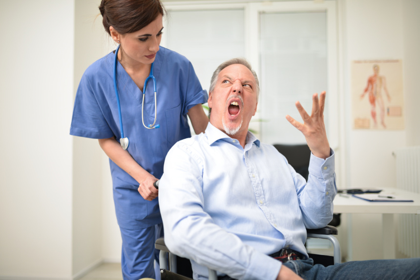 A wheelchair-bound, angry patient yells at a nurse.
