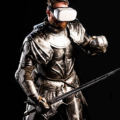 A man in a suit of armor and a medieval sword wears VR goggles.