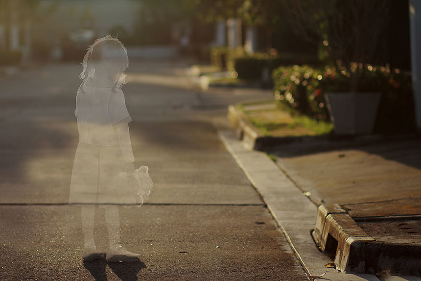 Transparent outline of a young girl stands in an empty street. Signifies a missing child.