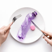 Person cutting through a discarded plastic bottle with a fork and knife.