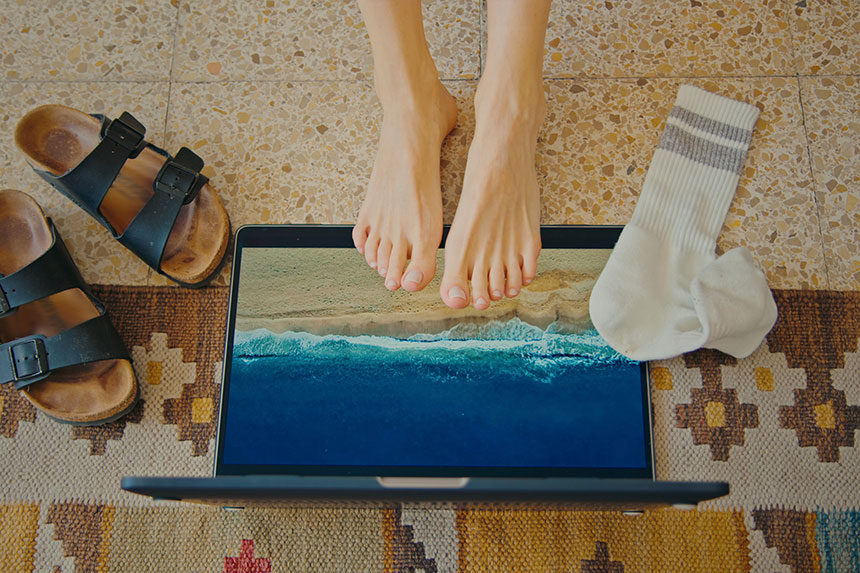 Feet on a laptop that has a beach on its screen