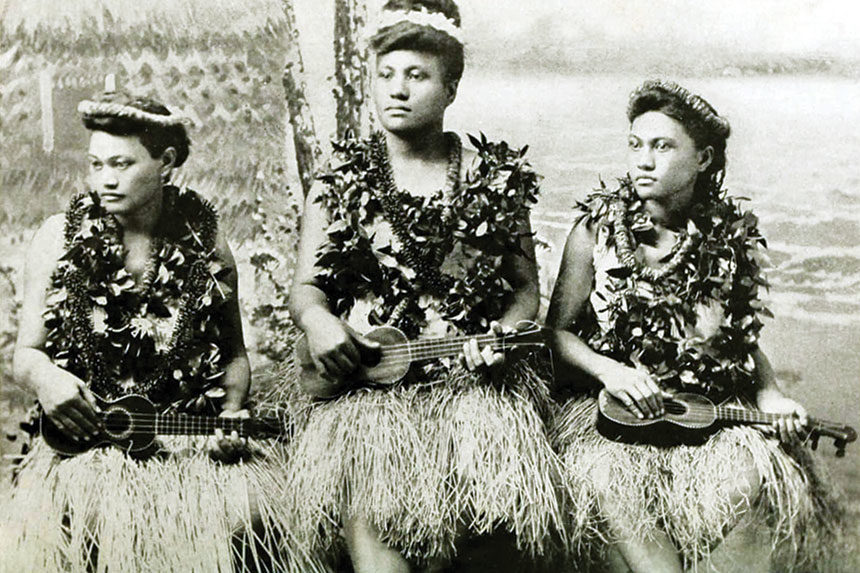 Women in traditional Hawaiian dress play their ukuleles