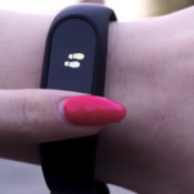 Finger with a painted nail resting on a wrist pedometer.