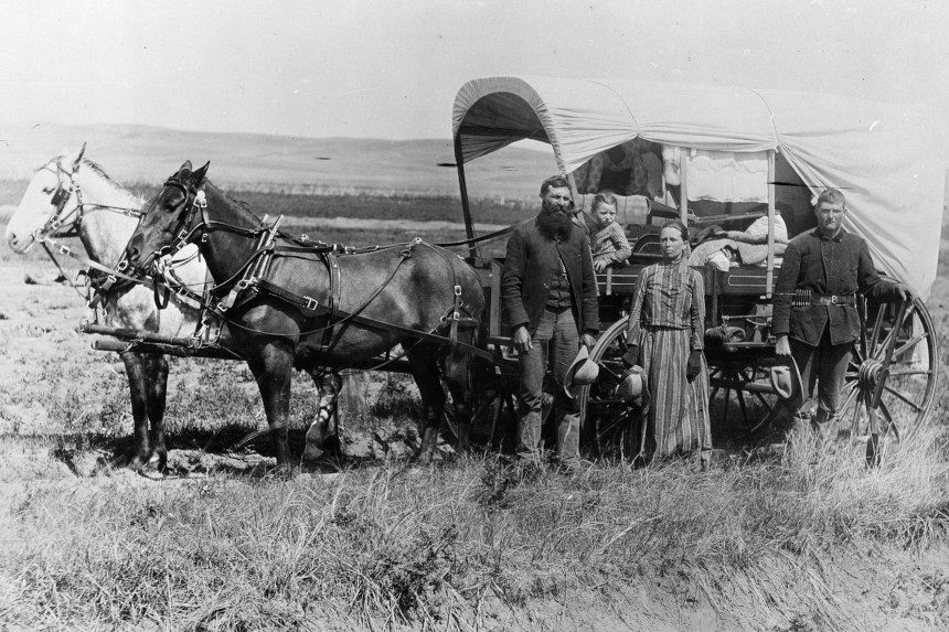 American migrant family poses with their horse-drawn covered wagon.
