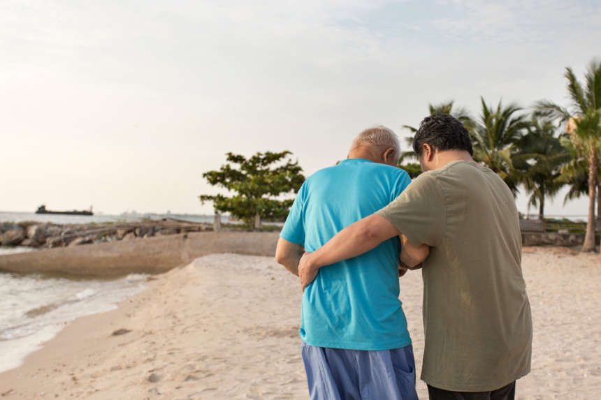 A senior citizen with Alzheimer's and his son walking together on the beach.