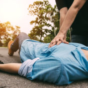 Man performing CPR on a heart attack victim in the middle of a paved street.