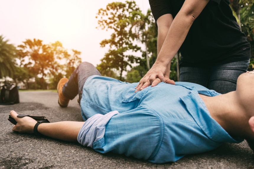 Man performing CPR on a heart attack victim in the middle of a paved street.