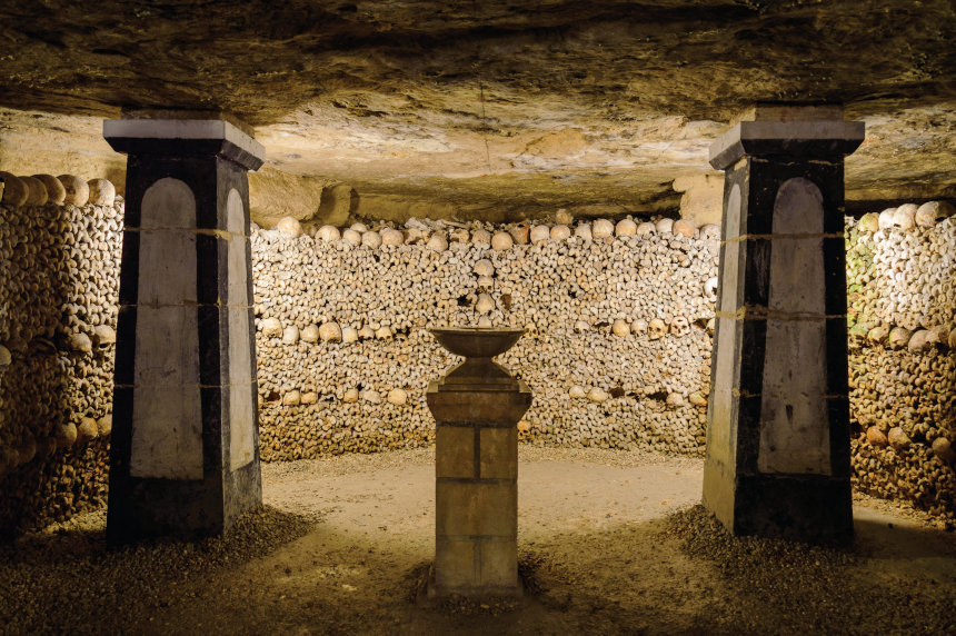 Skulls line the wall around an alter in an underground catacomb.