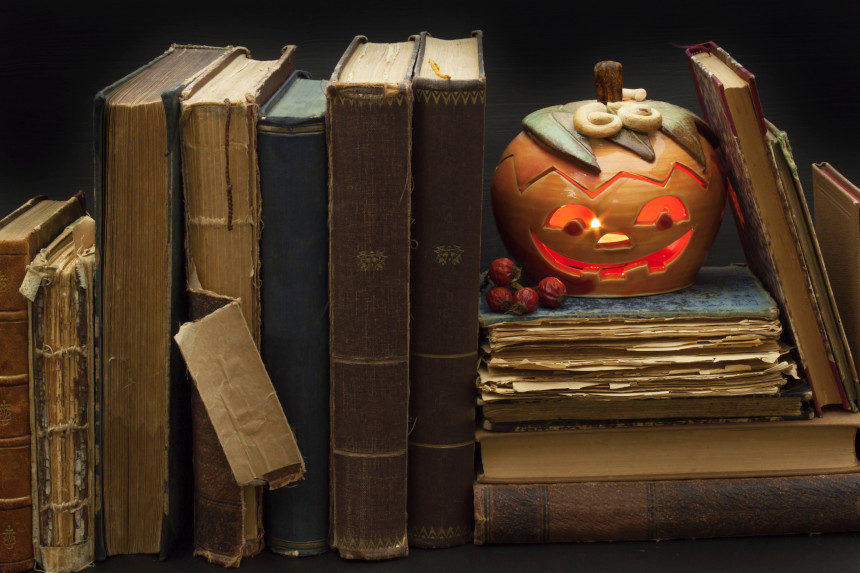 A grinning Jack-o'-Lantern rests on dusty old books.