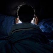 A child looking at a tablet while under the sheets