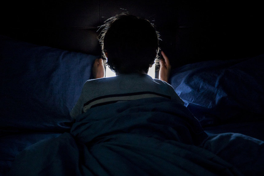 A child looking at a tablet while under the sheets