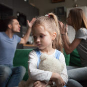 Two parents arguing while their anxious child hugs a stuffed doll.