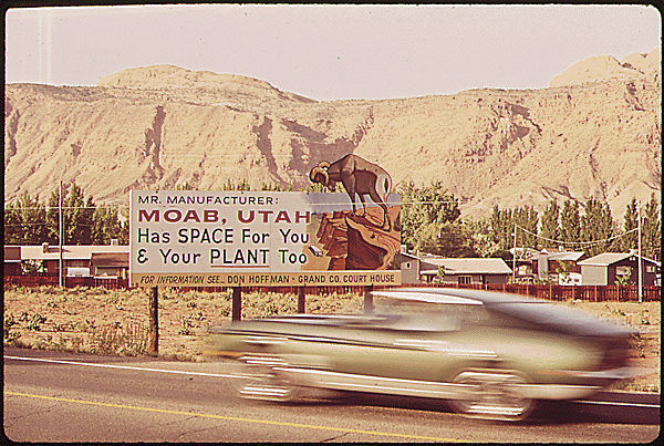 Cars drive by a billboard advertising space for industrial plants near Moab, Utah