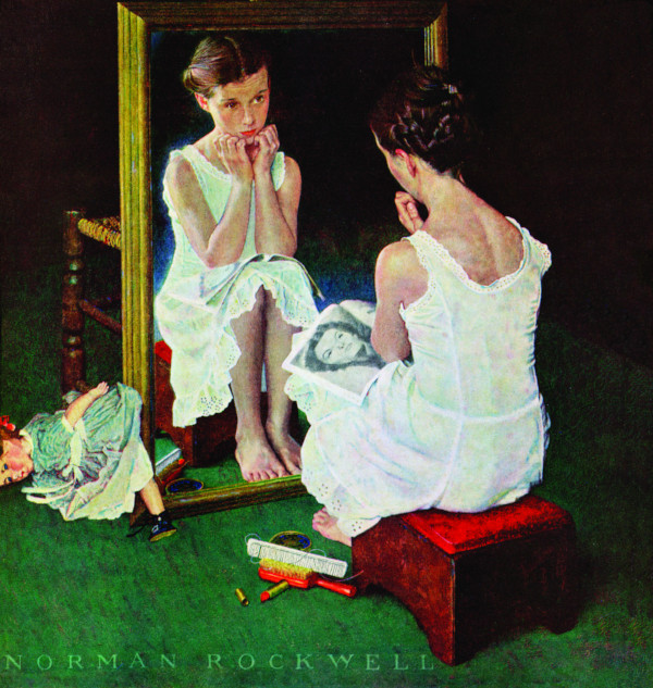 A young girl looks at herself in the mirror, comparing her looks to the Hollywood actress in her magazine.