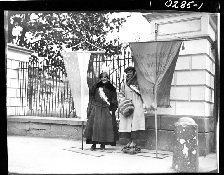 Two members of the Silent Sentinels pose in front of government buildings during a suffrage march