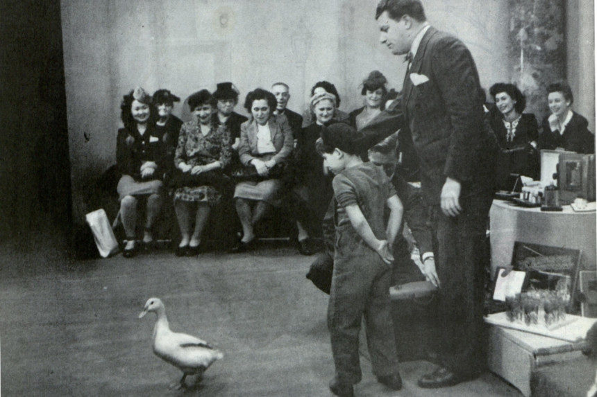 A young boy and a television host stare at a duck during a live studio recording.