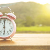 An old fashioned alarm clock on a wooden table outside in the morning sun.
