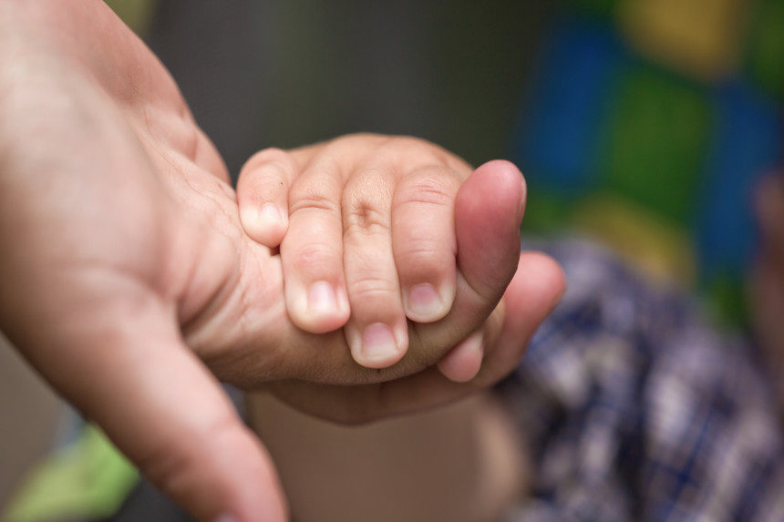 A toddler holding their parent's hand.