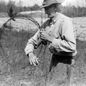 Farmer putting up barbed wire fence.