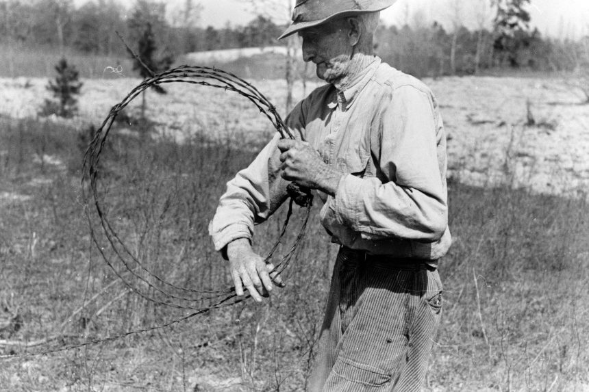 Farmer putting up barbed wire fence.