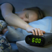 Woman hitting the snooze button on her alarm clock