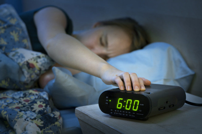 Woman hitting the snooze button on her alarm clock