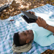 Man reading a digital tablet outside on a blanket.