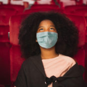 Kid watching a movie in a theatre while wearing a mask.