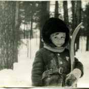 A boy with a ski stands in a snow covered forest in winter.