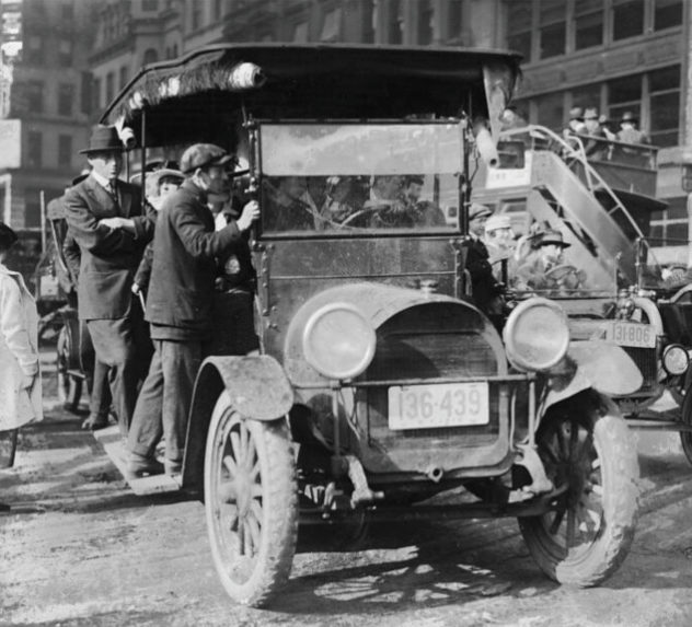 Men riding an overcrowded jitney car in New York City.