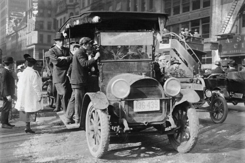 Men riding an overcrowded jitney car in New York City.