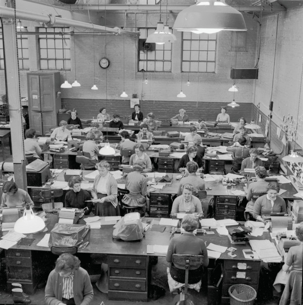 1950s, Historical. A typing pool in a factory. Female secretarial staff sitting at large desks at work in an open plan, high celling area of a factory building.. Image shot 1950. Exact date unknown.