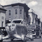 A vintage automobile with large wheels drives down a street in 1947.