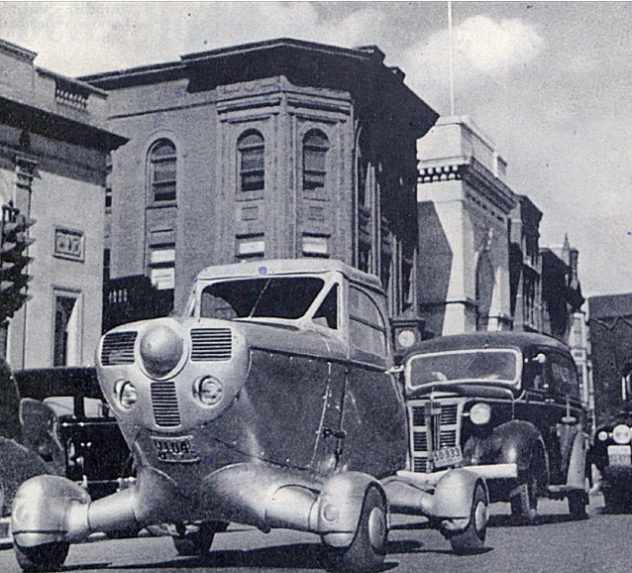 A vintage automobile with large wheels drives down a street in 1947.