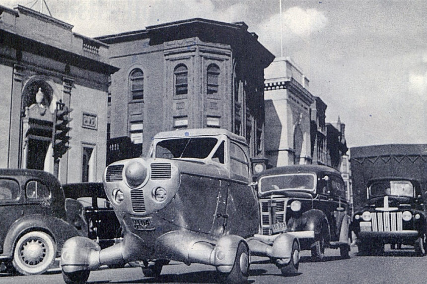 A vintage automobile with large wheels drives down a street in 1947.