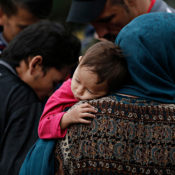 A small Afghan child holds onto their mother as they wait with other refugees.