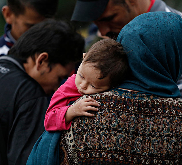 A small Afghan child holds onto their mother as they wait with other refugees.